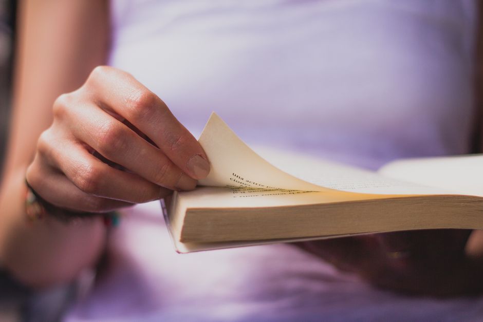 Caucasian woman in a contemplative mood, reading a book next to soft pink petals indoors.