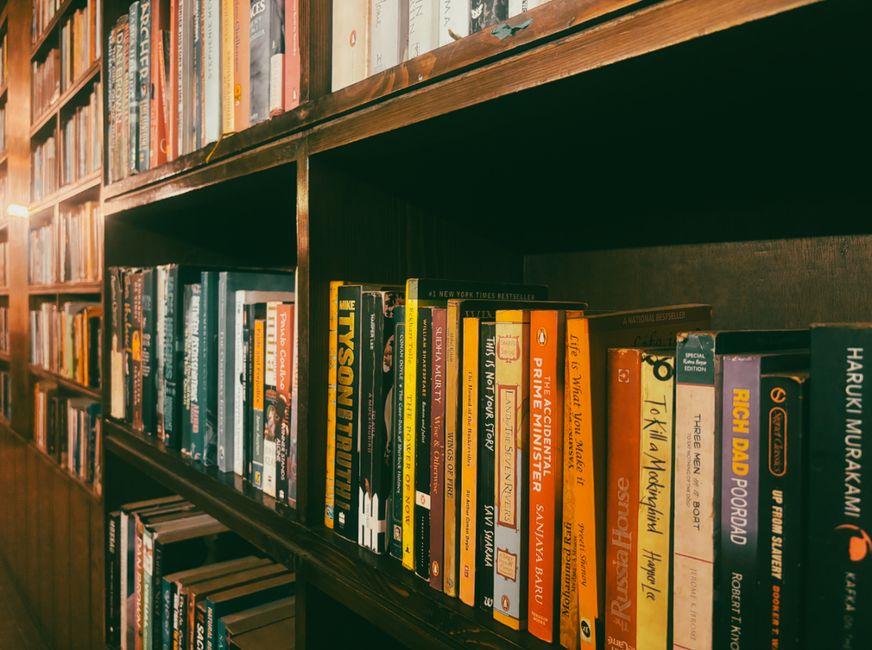 A close-up view of various colorful books lined up on a rustic wooden shelf indoors.