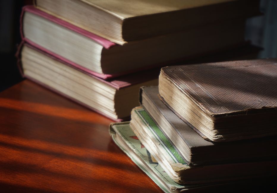 A close-up of vintage books stacked on a wooden table, showcasing aged pages and covers.