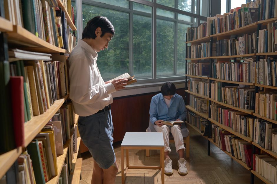 Two individuals reading in a quiet library setting with abundant natural light.