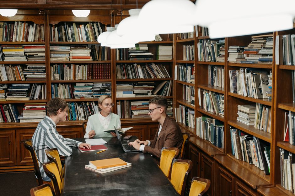 Two individuals reading in a quiet library setting with abundant natural light.
